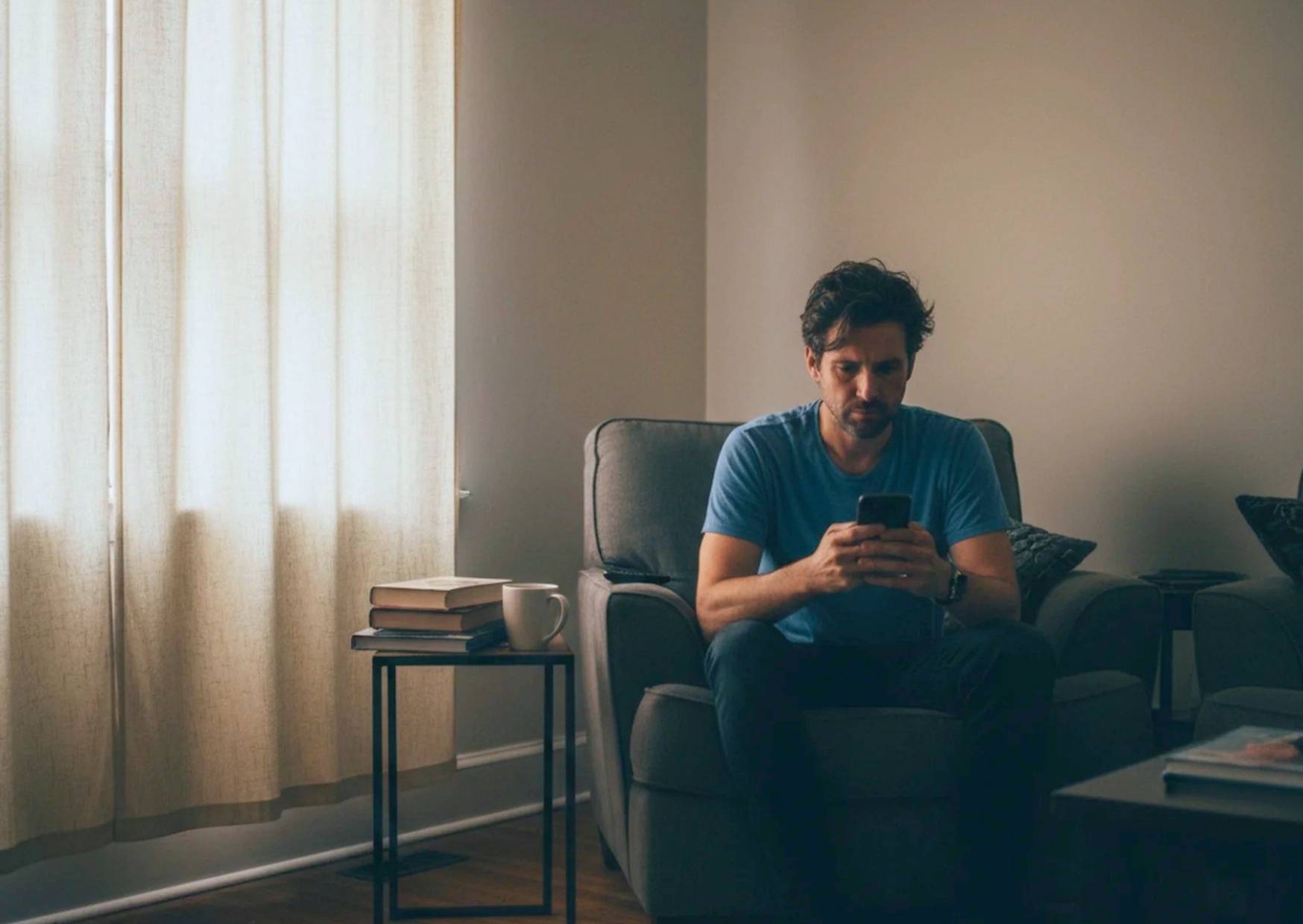 A man sitting alone looking at his phone with a disconnected expression