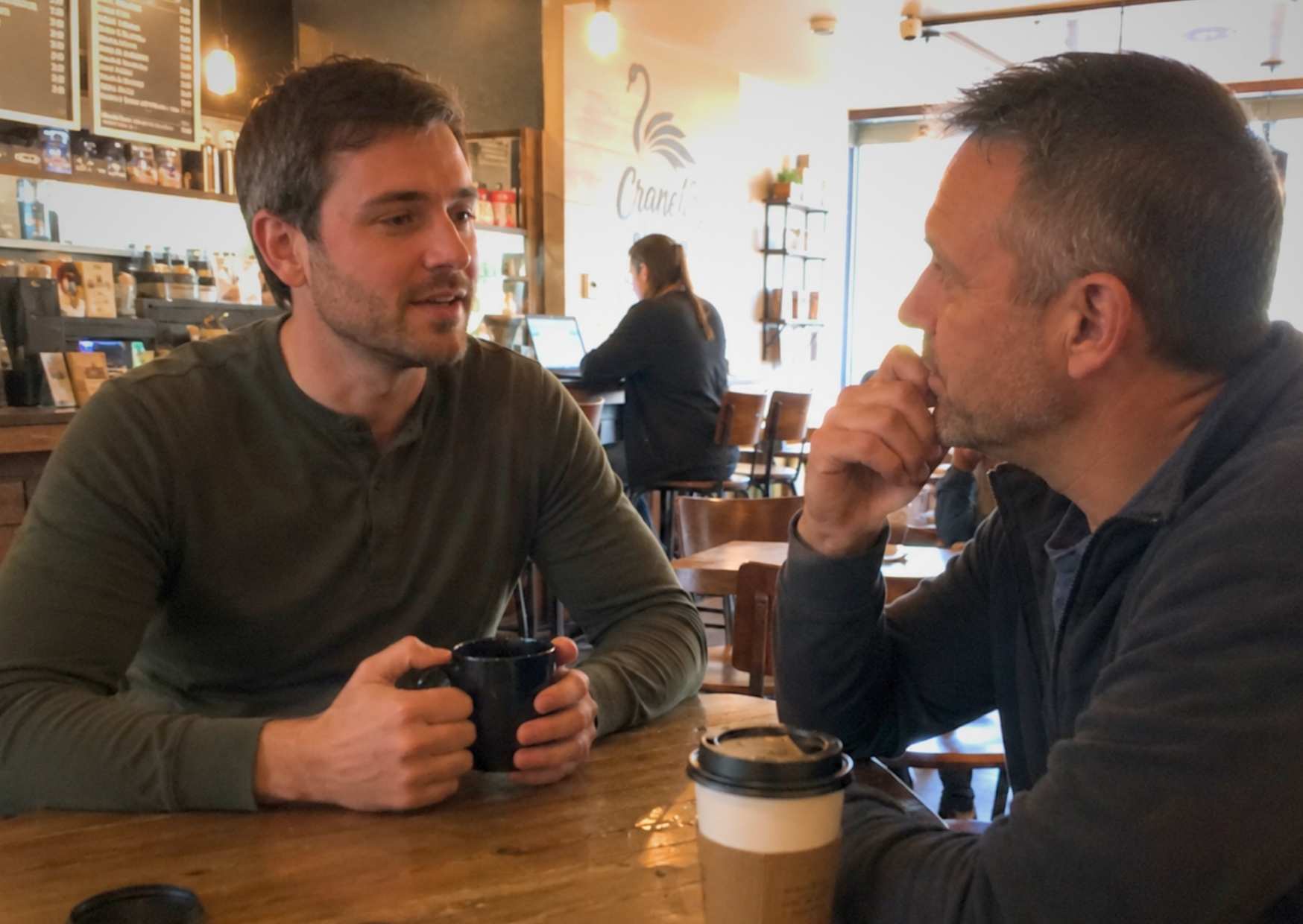 Two people in deep conversation at a coffee shop, one leaning in